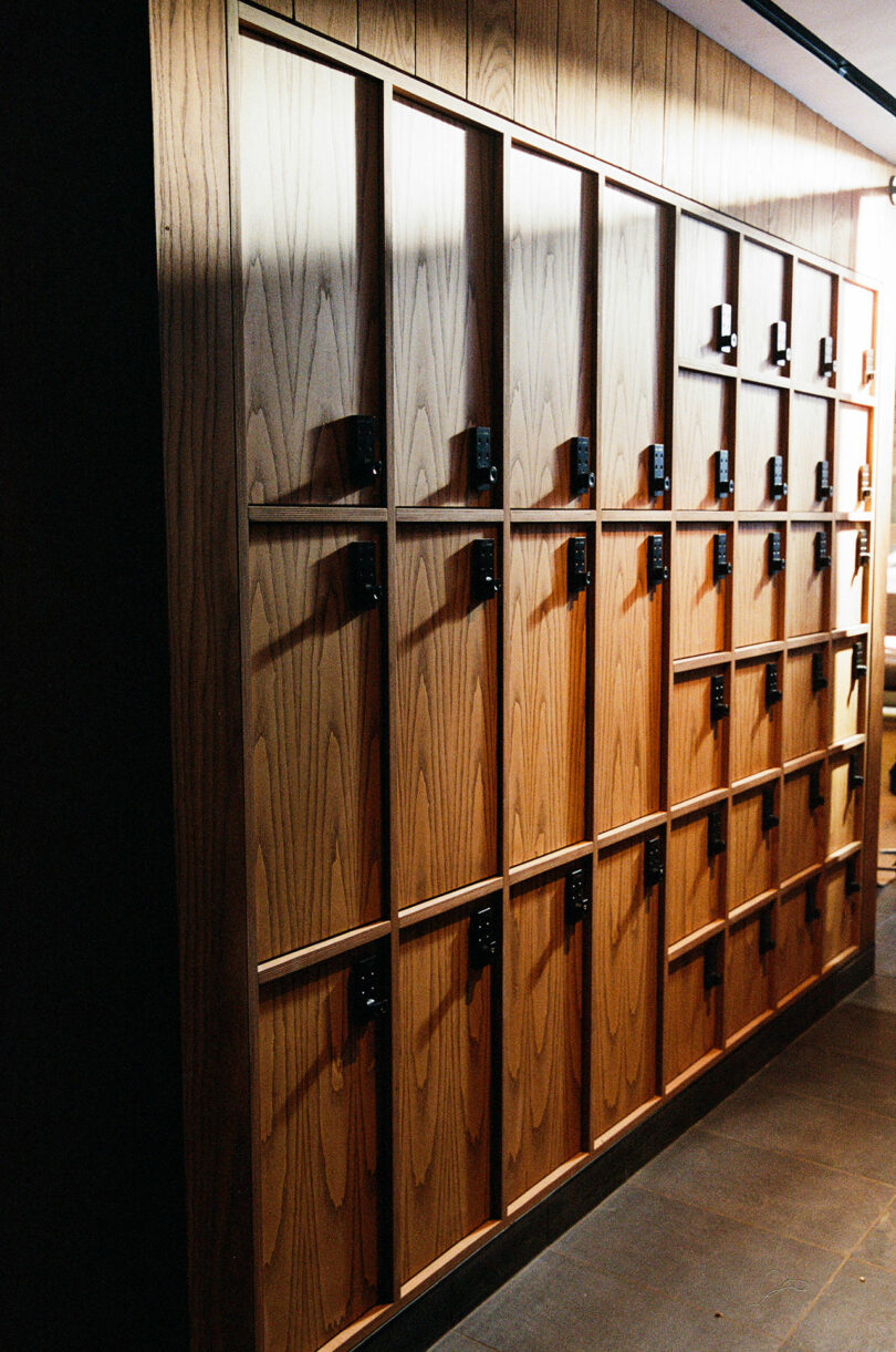 A row of wooden lockers with black locks is arranged against a wall in a well-lit interior space.