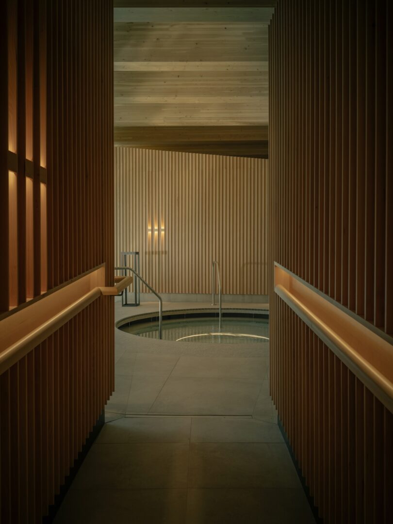 Indoor spa area with wooden slats, warm lighting, and a small circular pool with metal handrails at the center.
