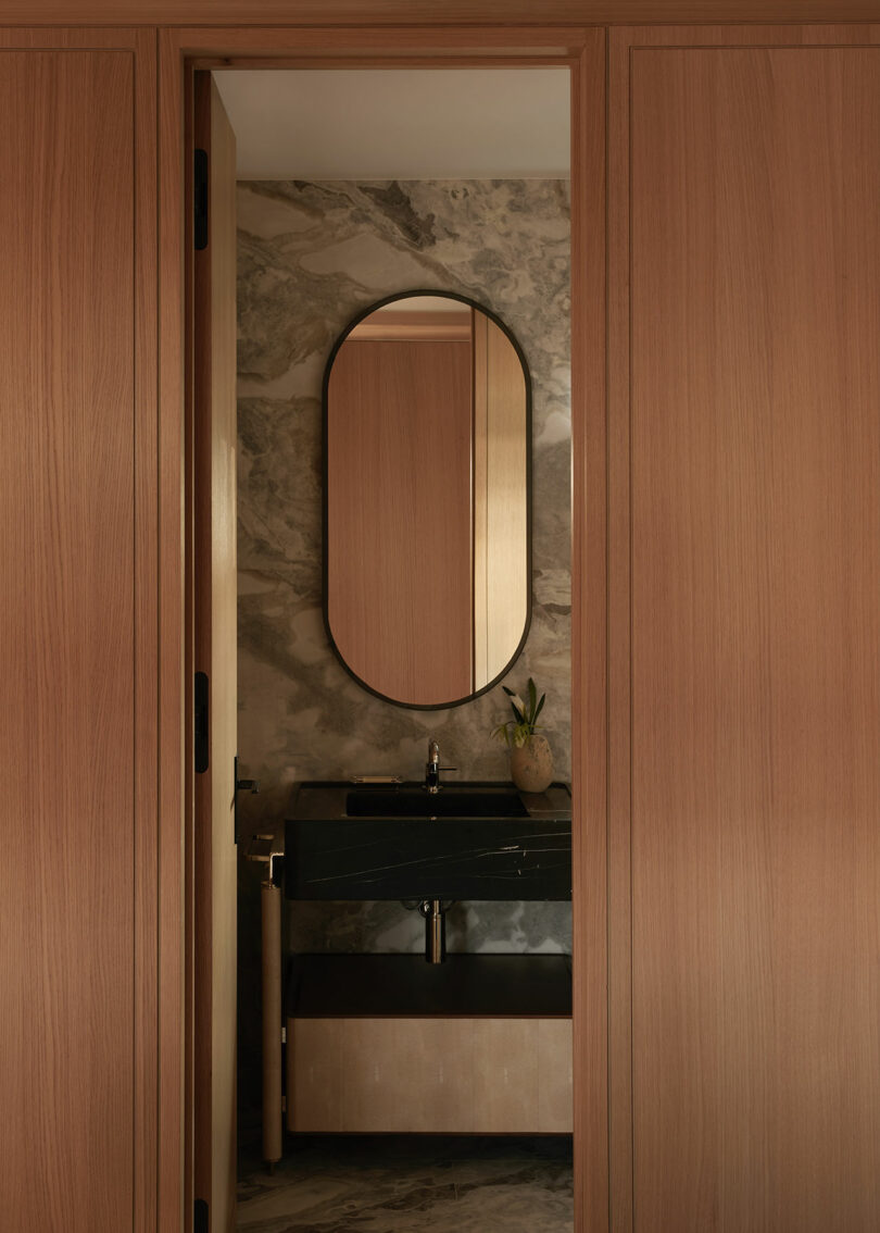 Modern kitchen with marble countertop, built-in cabinets, and decorative plants, featuring large windows with ocean views and warm sunlight filtering into the room.