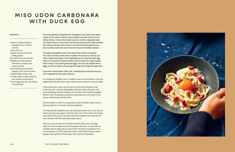 A bowl of miso udon carbonara topped with a raw duck egg yolk, shredded cheese, and small pieces of bacon sits on a dark blue surface, promising a rich taste experience alongside the recipe and instructions.