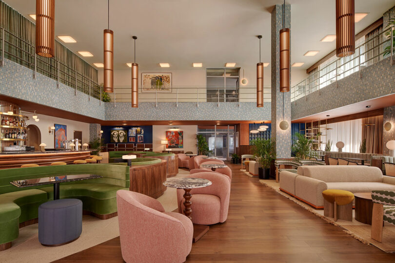 Modern hotel lobby at Municipal Grand with mid-century style furniture, including sofas, armchairs, and a circular bar, featuring warm lighting and large windows.