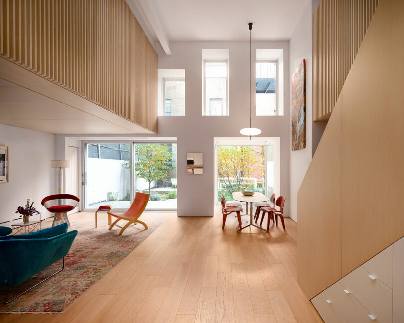 Modern living and dining area with light wood floors, large windows, mid-century furniture, a rug, and a view of a small outdoor garden.