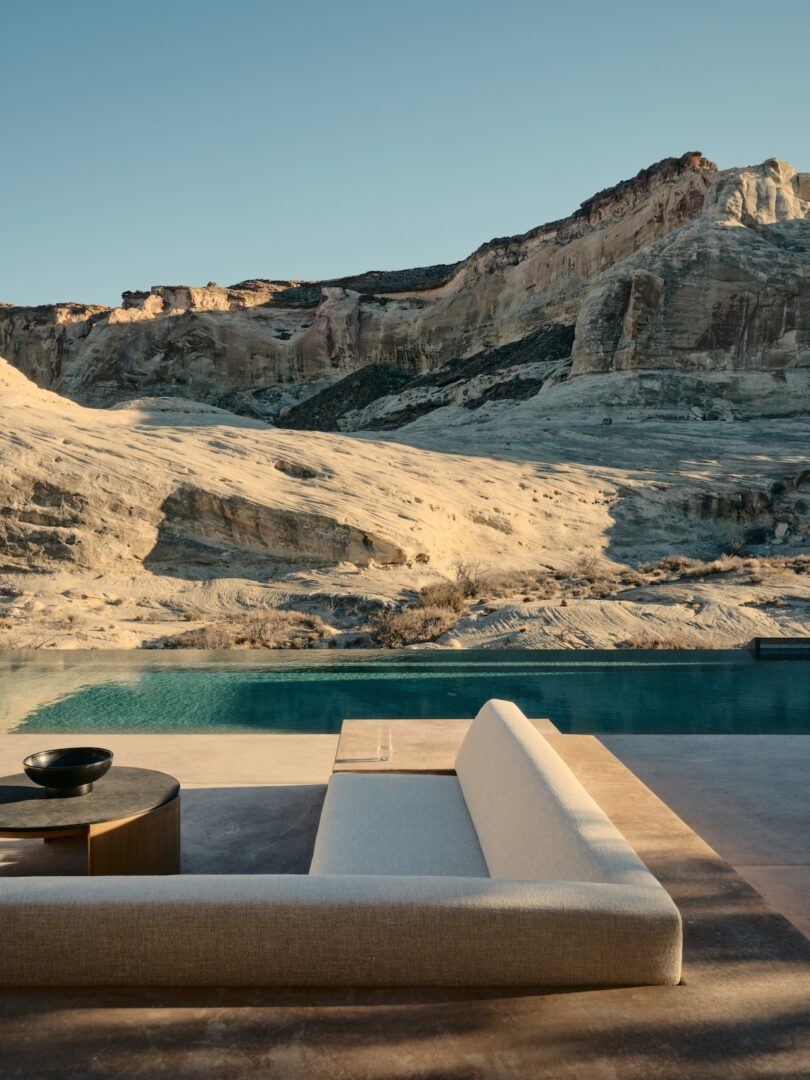 A modern outdoor sofa and table sit beside a pool overlooking rocky desert cliffs under a clear sky.
