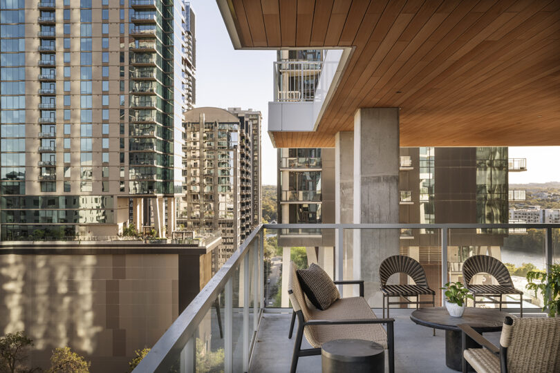 Modern Roost Rainey apartment balcony with a cozy seating area, lush potted plants, and stunning city high-rise buildings in the background.