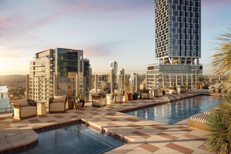 Rooftop pool area at Roost Rainey, featuring lounge chairs, planters, and city skyscrapers in the background at sunset.