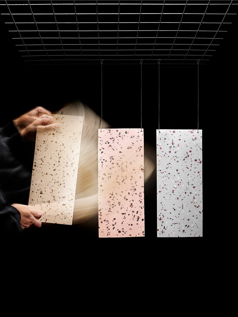 A hand is shown moving three rectangular Tarkett panels with speckled patterns, suspended from a grid against a black background.