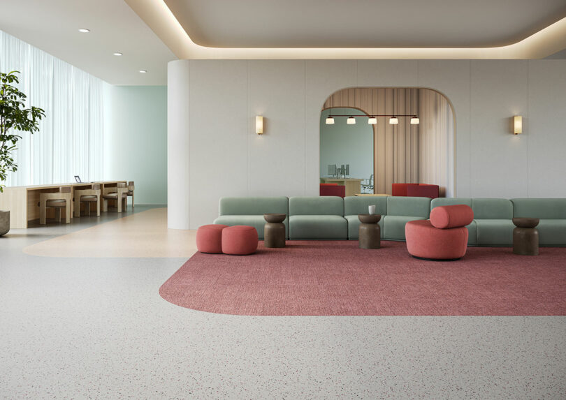 Modern lounge area with a green sofa, pink ottomans, small tables, and a large arch mirror on the wall; Tarkett flooring complements the space as natural light streams in through tall windows.