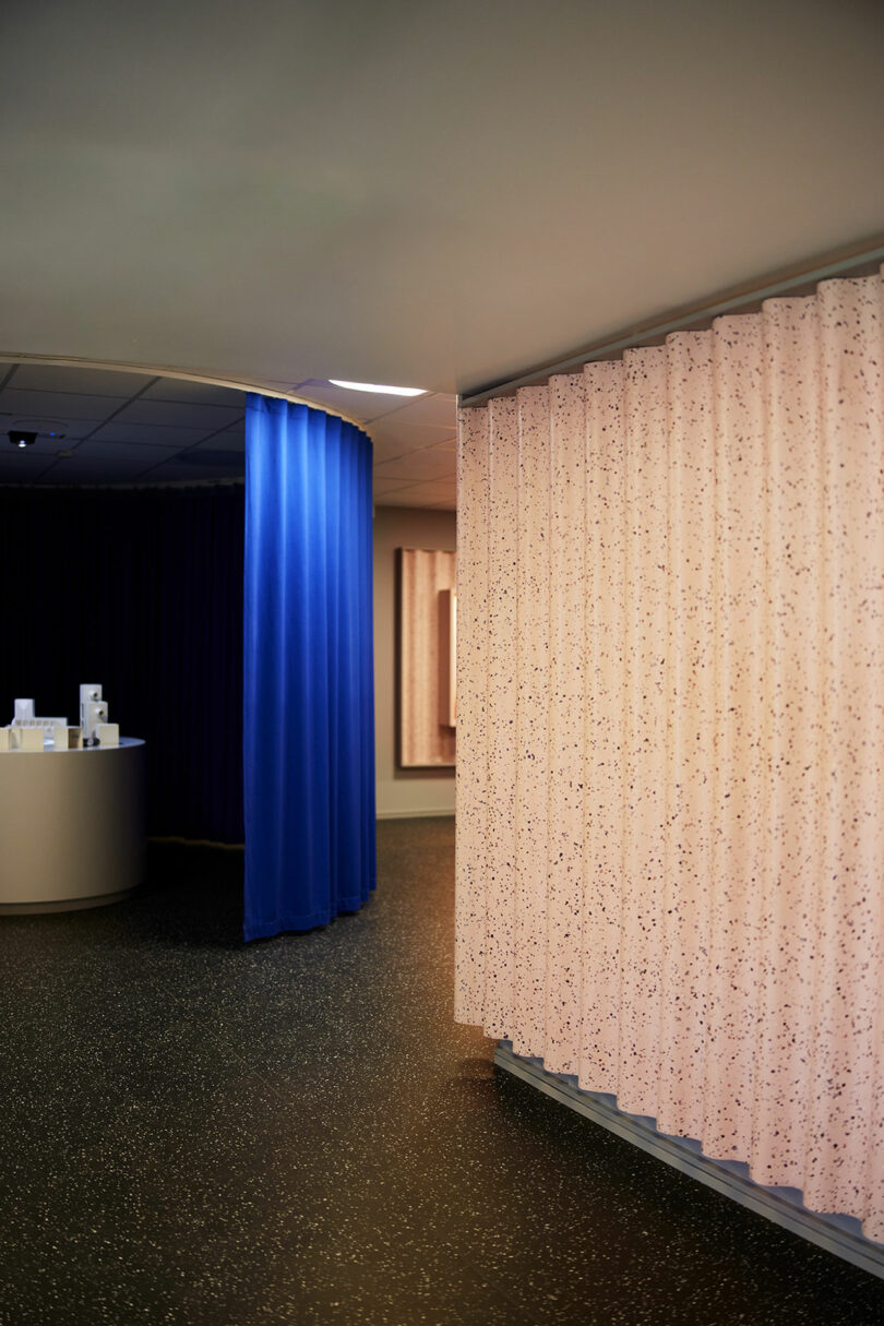 Partition curtains in pink and blue create separate areas in a modern interior with Tarkett speckled flooring and a curved display counter in the background.