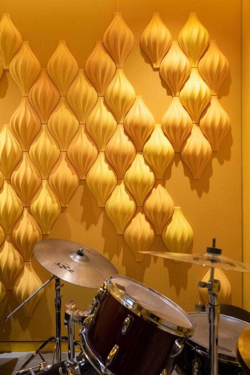 A drum set is positioned in front of a yellow wall decorated with three-dimensional, leaf-shaped wall panels.