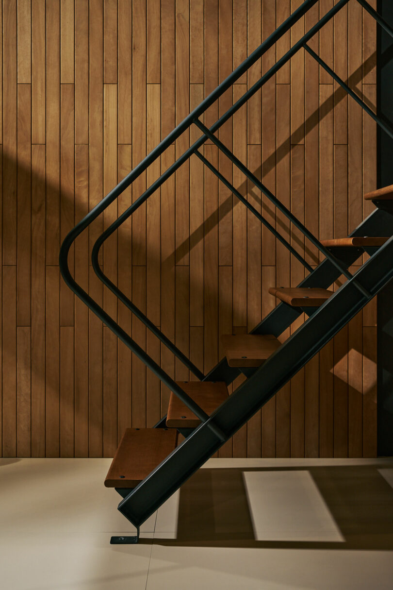 A modern staircase with dark metal railing and wooden steps stands against a wall with vertical wooden panels.