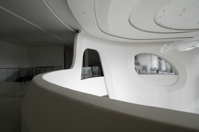 Curved white interior wall with oval and rounded openings, showcasing a modern minimalist design where confluence of form and soft natural lighting creates a serene atmosphere.