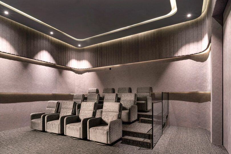 A small, modern home theater room showcases a confluence of style and comfort with two tiers of gray upholstered seats, soft wall panels, and recessed ceiling lighting.