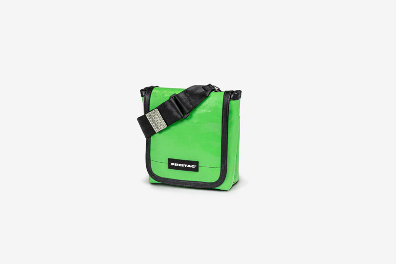 A small green shoulder bag with a black adjustable strap and a label reading "FREITAG" on the front.