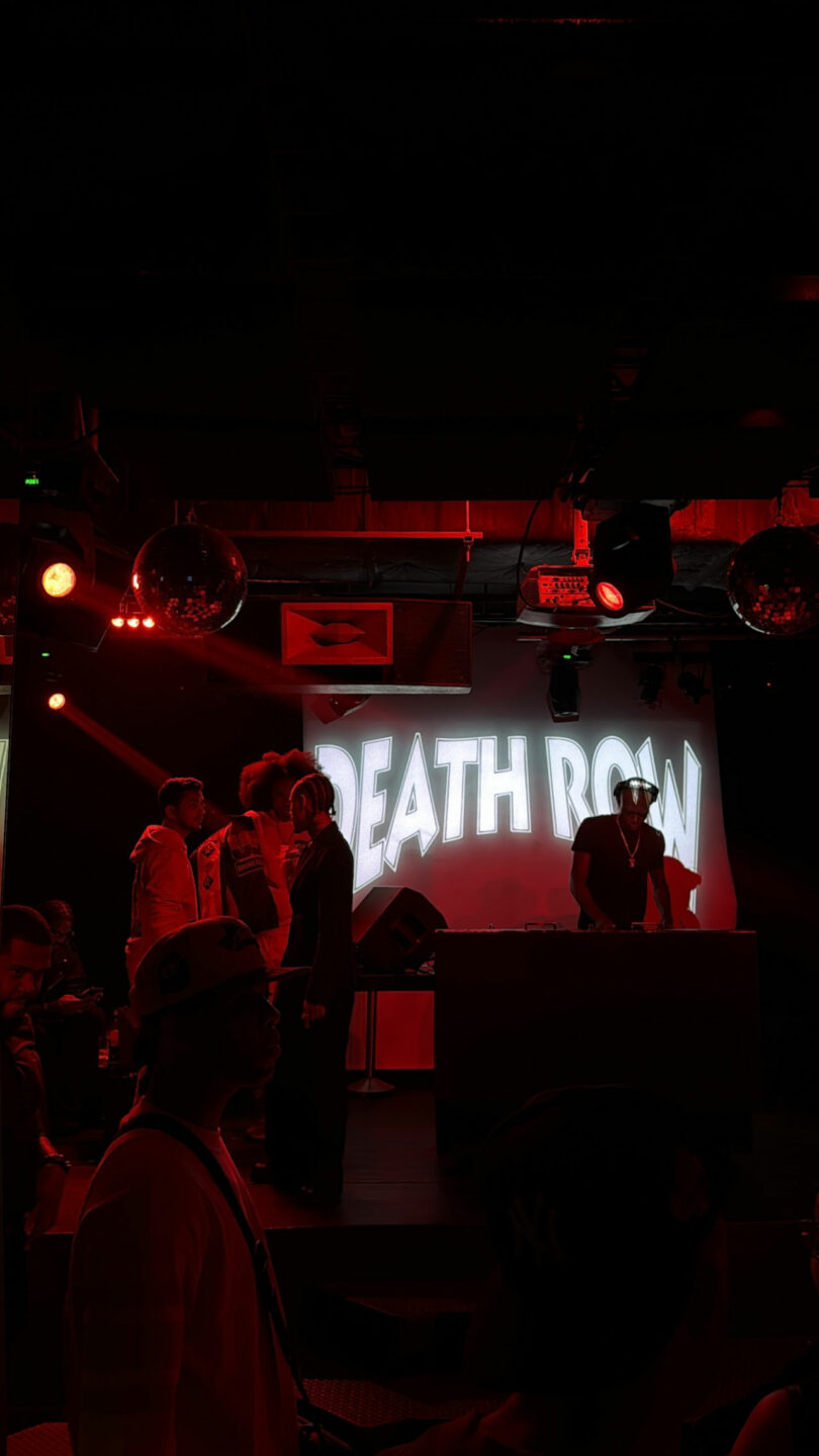 A group of people stand near a DJ booth under red lights with "DEATH ROW" projected in large white letters on the screen behind them, capturing the energy of a Friday Five event.