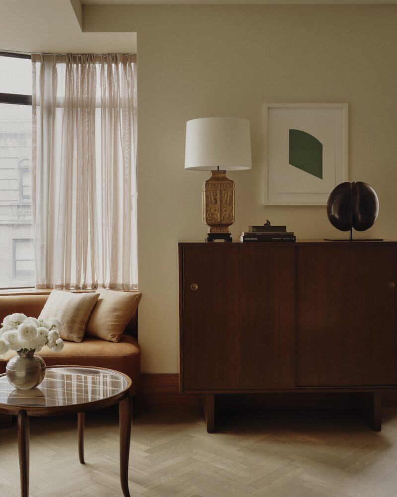 Heavy figured Khaya mahogany runs through the apartment as a continuous horizontal datum, becoming banquette seating in one room, cabinetry in another, and a lighted art plinth elsewhere.