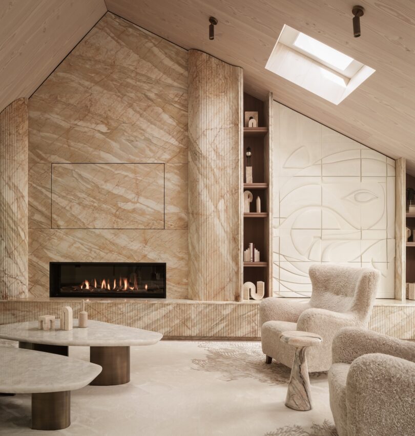 Modern living room with light stone walls, built-in fireplace, abstract wall art, sculptural shelves, plush chairs, and nested coffee tables under a skylight.