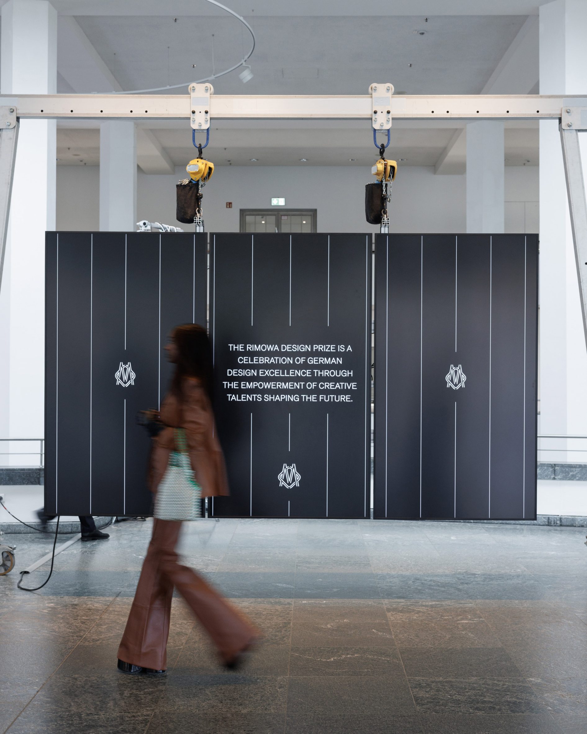 Visitor walking past the Rimowa Design Prize exhibition installation in a large gallery space