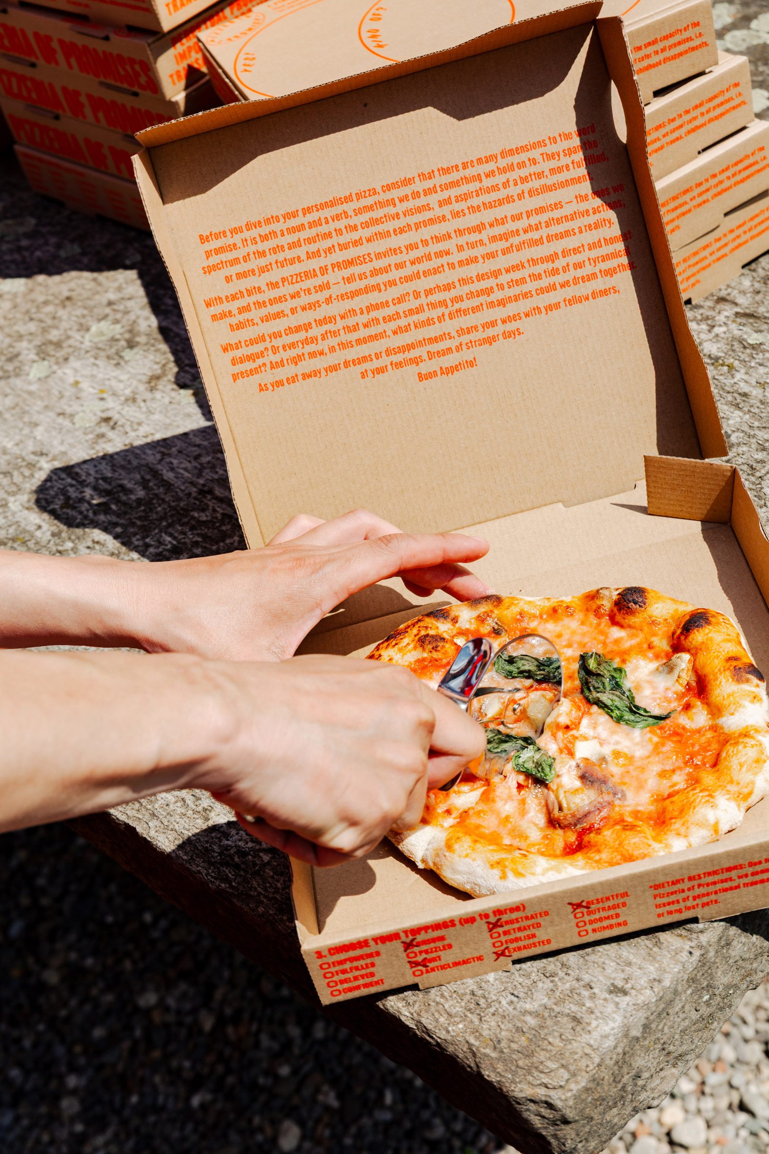 Photo of a person slicing into an Italian pizza in a box decorated with bright red text