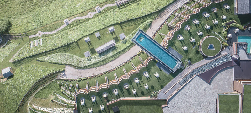 Aerial view of a terraced outdoor area with a linear pool, sun loungers, greenery, footpaths, and modern landscaping features, reflecting the innovative design seen in the Hotel Hubertus spa expansion.