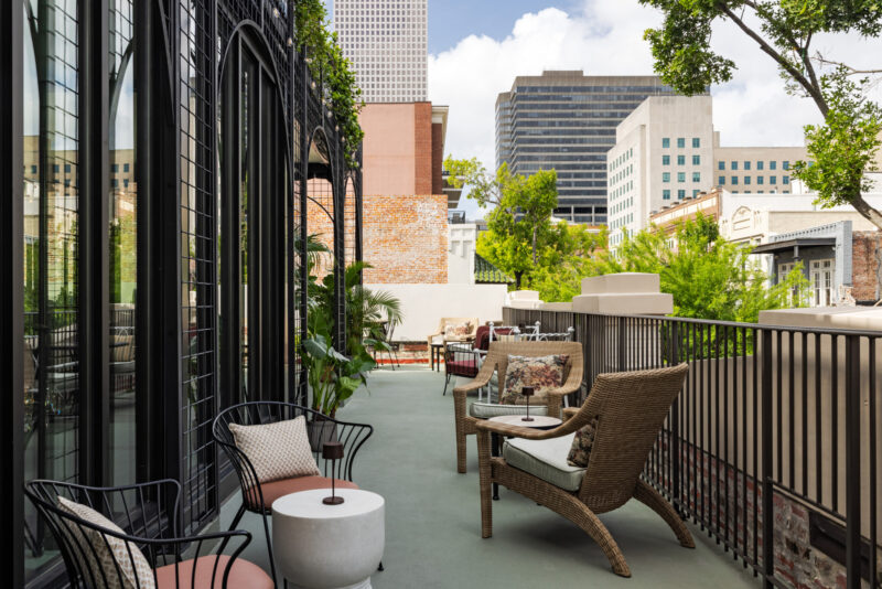 Outdoor terrace with wicker and metal chairs, small tables, potted plants, and city buildings in the background under a partly cloudy sky—an inviting setting reminiscent of Charles & Julia’s favorite urban escapes.