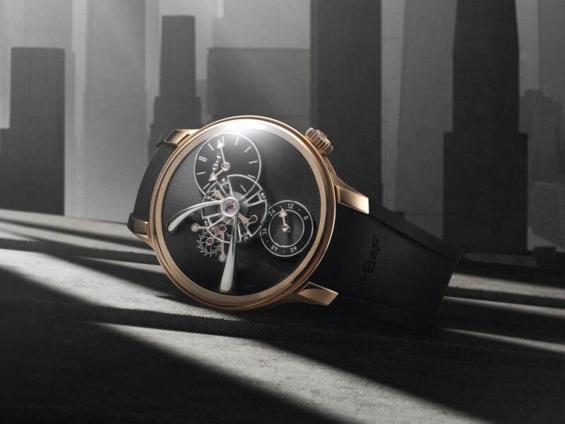 A luxury wristwatch with a black face and gold casing rests on a surface, with a modern cityscape and beams of light in the background.