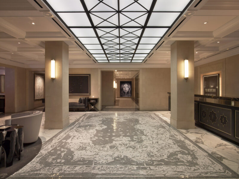 A spacious, elegant hotel lobby with marble floors, modern lighting, lounge seating, and framed artwork on the walls.