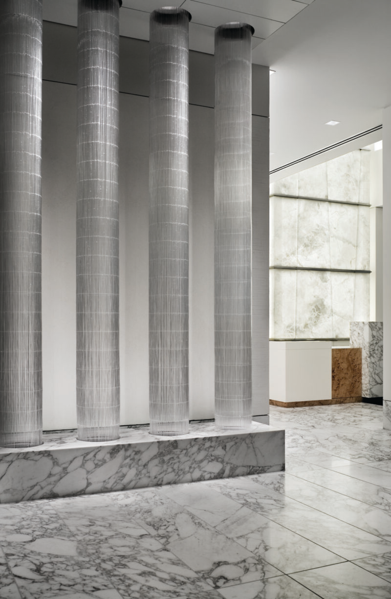 Modern interior with four tall cylindrical columns, marble floors and walls, and natural light from large frosted windows.