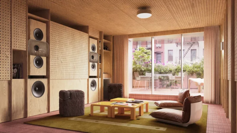 A modern living room with wood paneling, large speakers, low seating, a coffee table, and glass doors opening to a balcony with plants.