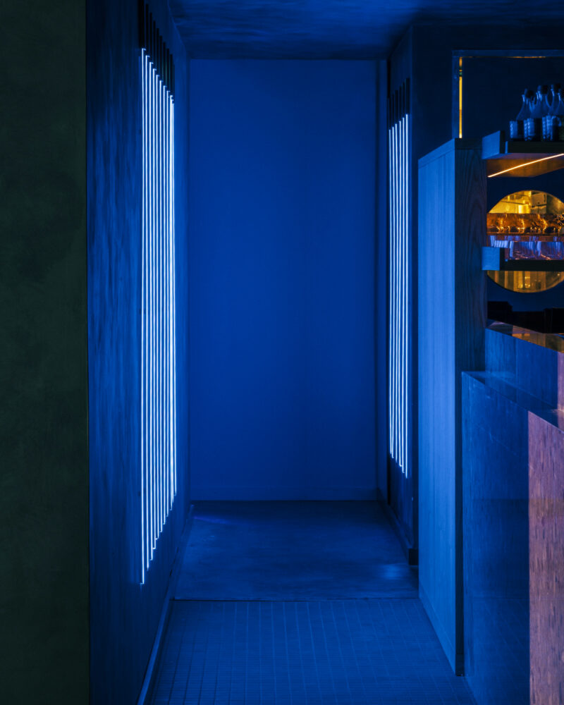 A narrow Japanese steakhouse hallway illuminated by vertical blue neon lights on the side walls.