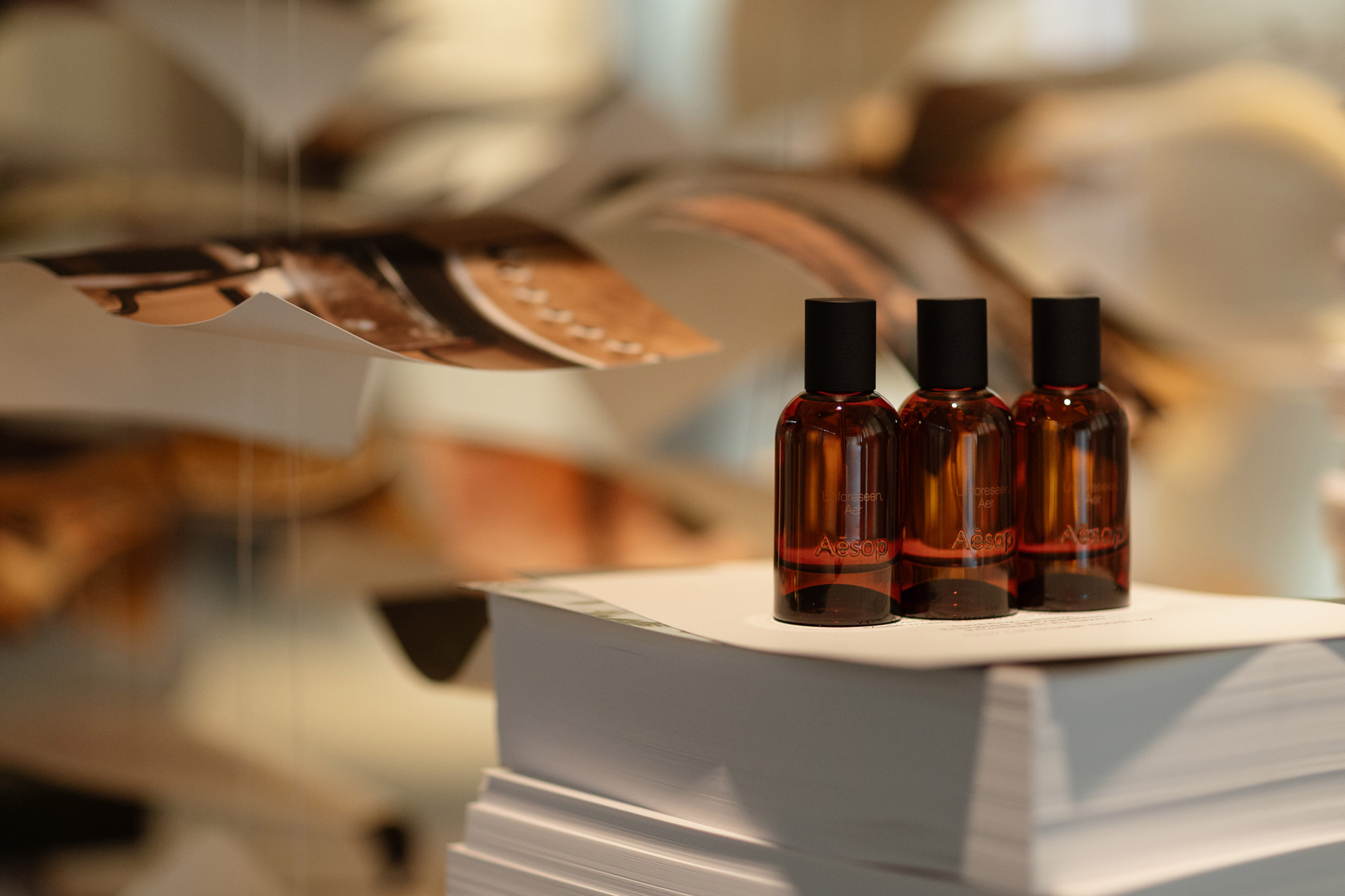 Three amber fragrance bottles sit on a stack of white paper beneath suspended sheets