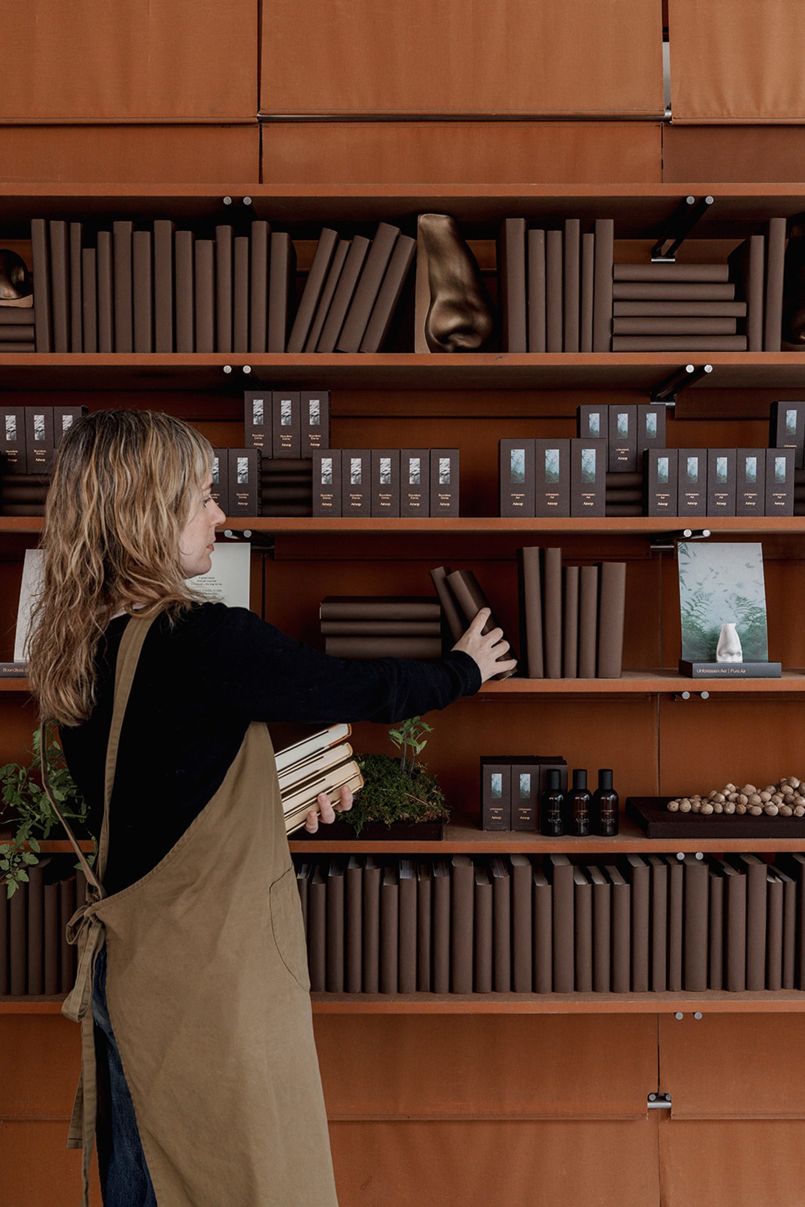A person arranging book-like fragrance packaging on wooden shelves