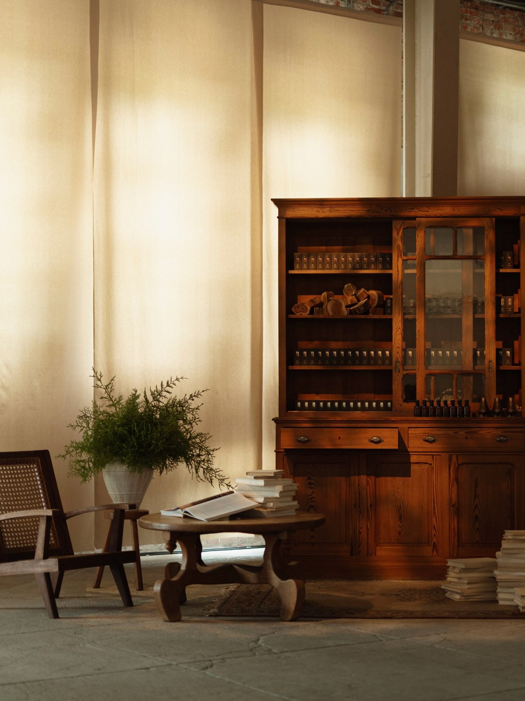 A wooden cabinet displays fragrance bottles and ingredients beside books and plants