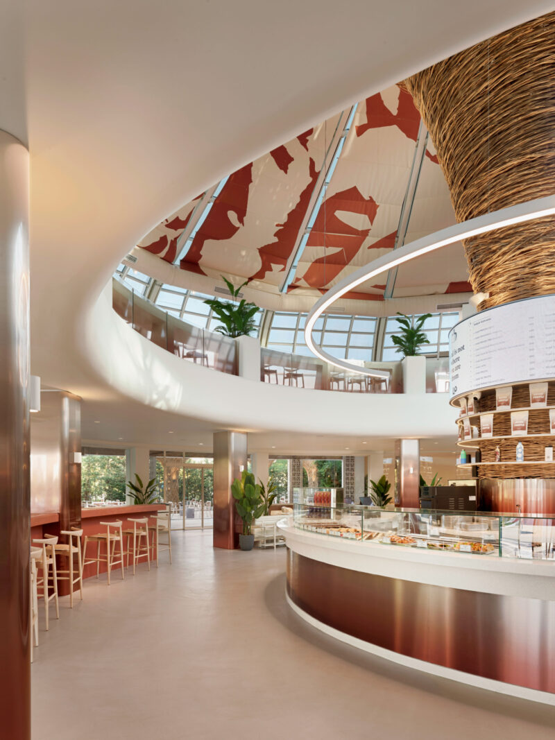 Modern Local People cafe interior featuring a circular curved service counter, a tiered display column, and a lofted seating area under a patterned glass dome ceiling.