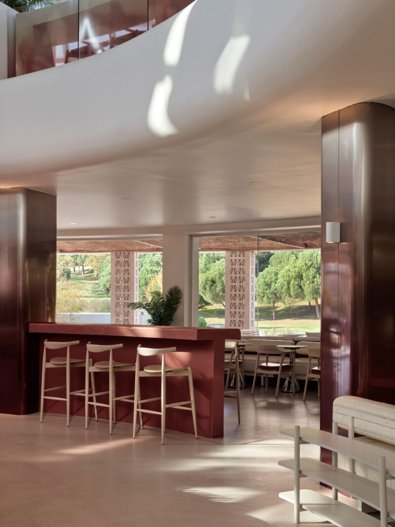 A modern Local People cafe lounge featuring a red bar, wooden stools, and large windows looking out onto a park.