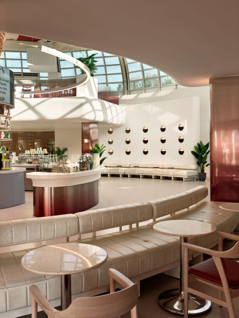 Modern cafe interior featuring a curved service counter, tufted bench seating, and a large glass-domed ceiling.