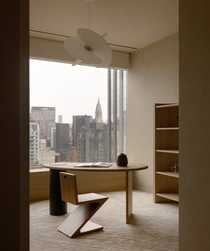 A desk and chair positioned in front of a window overlooking the New York City skyline.