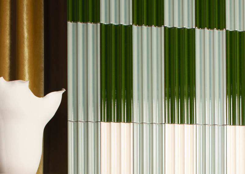 A wall covered in vertically ribbed tiles alternating between dark green and off-white, with a portion of a white curved object in the foreground.