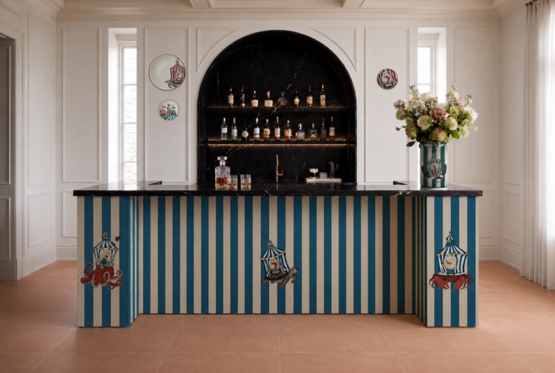 A home bar featuring a blue-and-white striped base decorated with circus-themed illustrations, topped with a black marble counter and a matching arched liquor shelf.